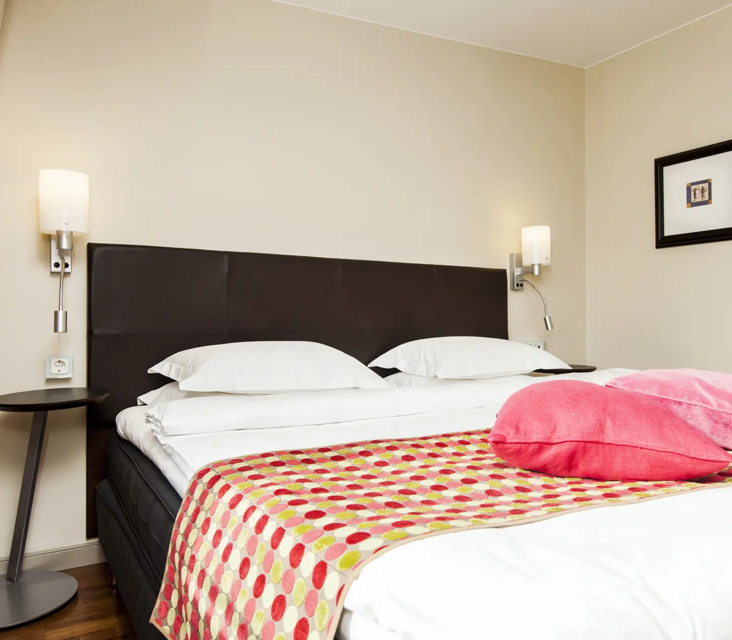 Hotellrum med säng, rosa kuddar och sänglampor