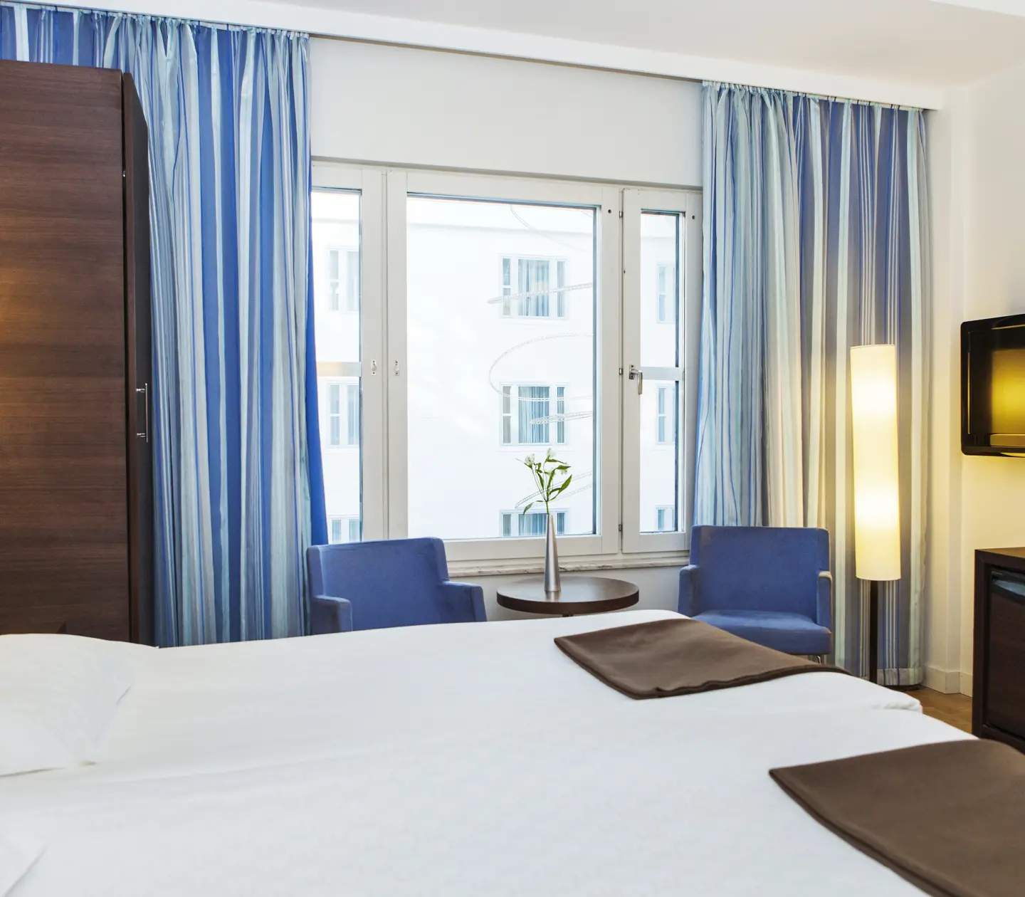 Ljust hotellrum med blå gardiner, blå fåtöljer och säng