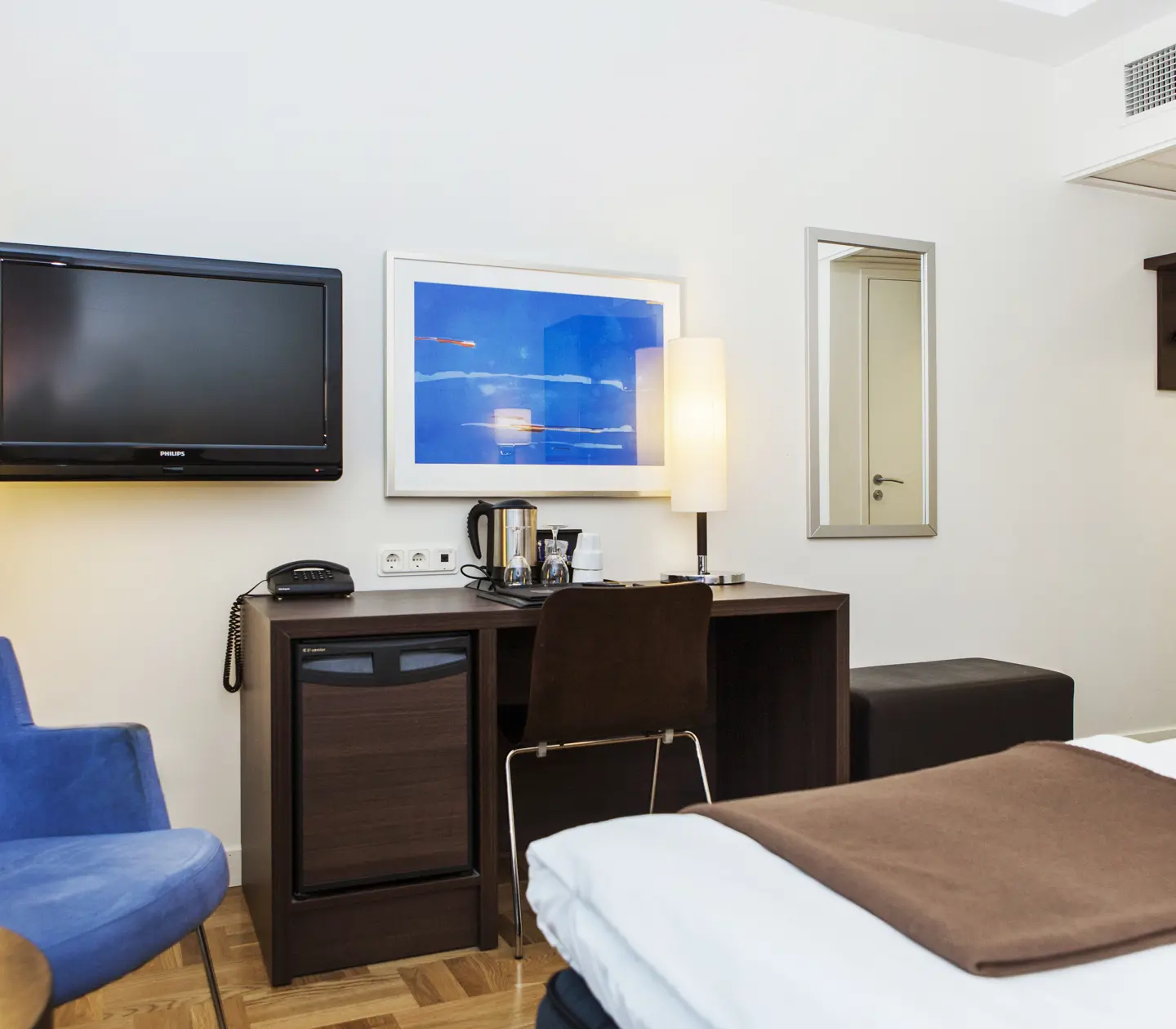 Ljust hotellrum med skrivbord, tv och blå fåtölj