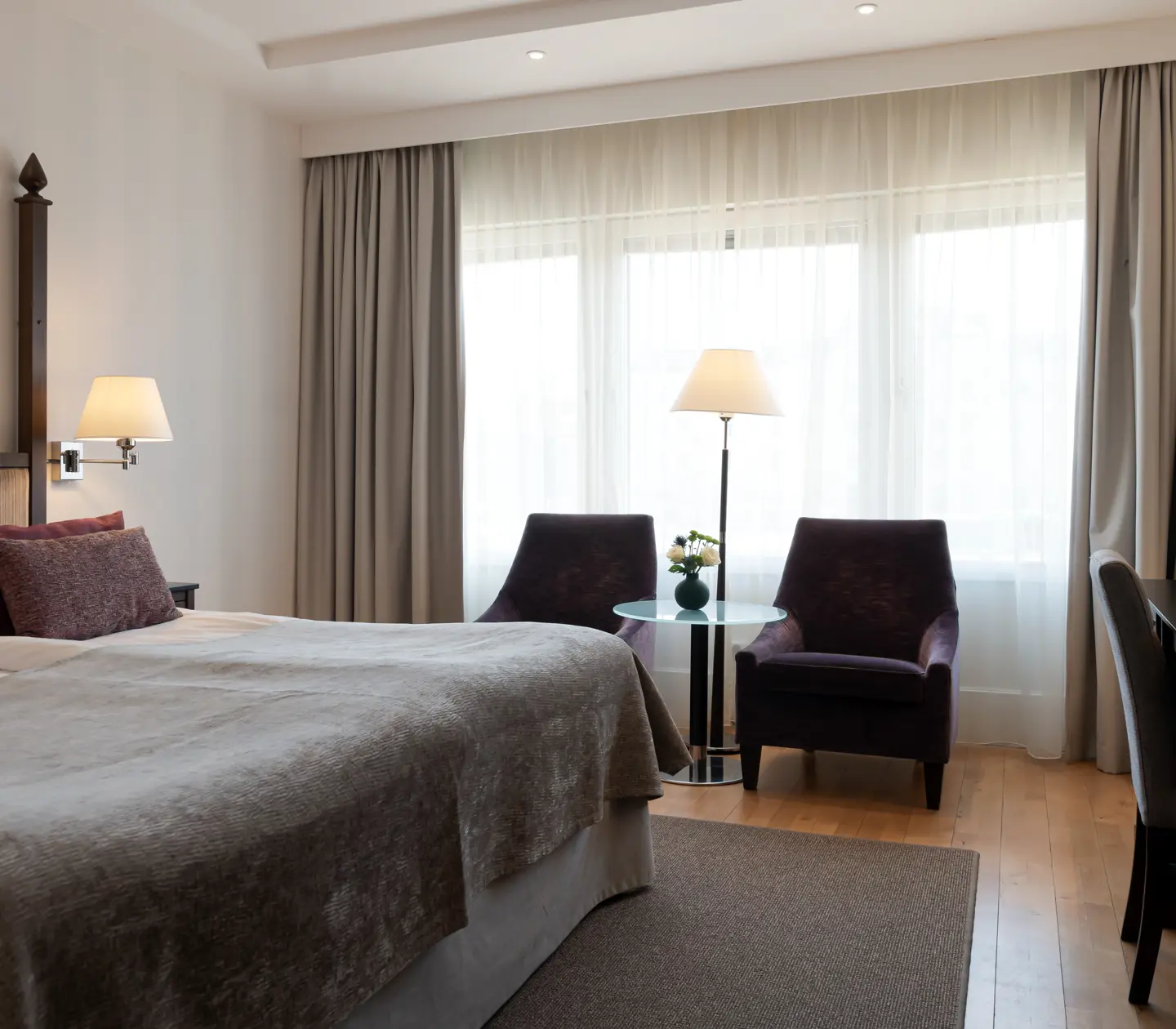 Ljust hotellrum med dubbelsäng, fåtöljer och fönster