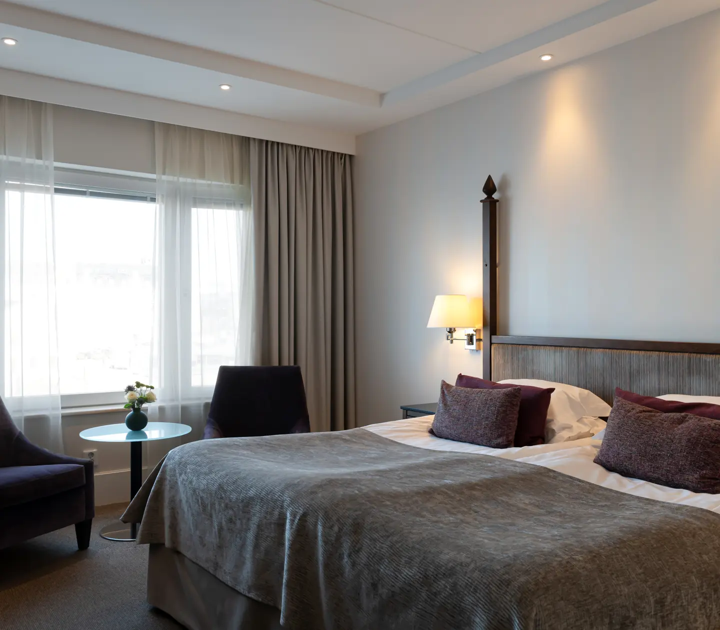 Ljust hotellrum med dubbelsäng, fåtöljer och fönster