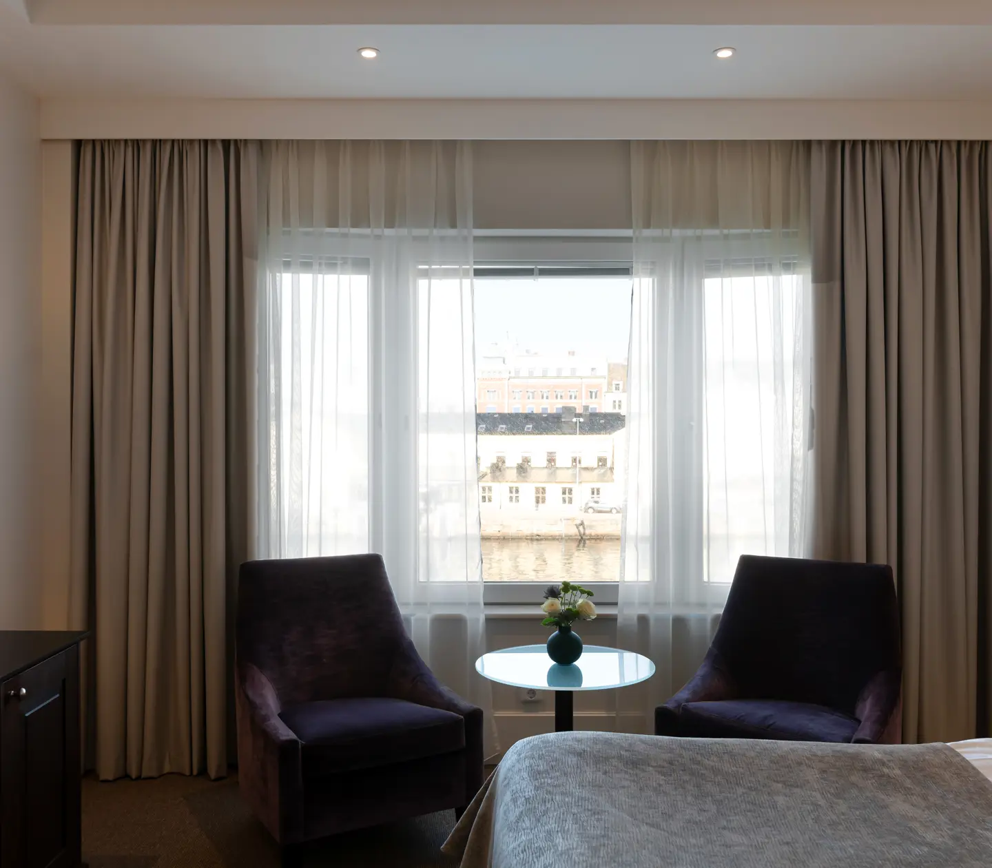 Ljust hotellrum med skrivbord, fåtöljer och fönster med utsikt över hamnen