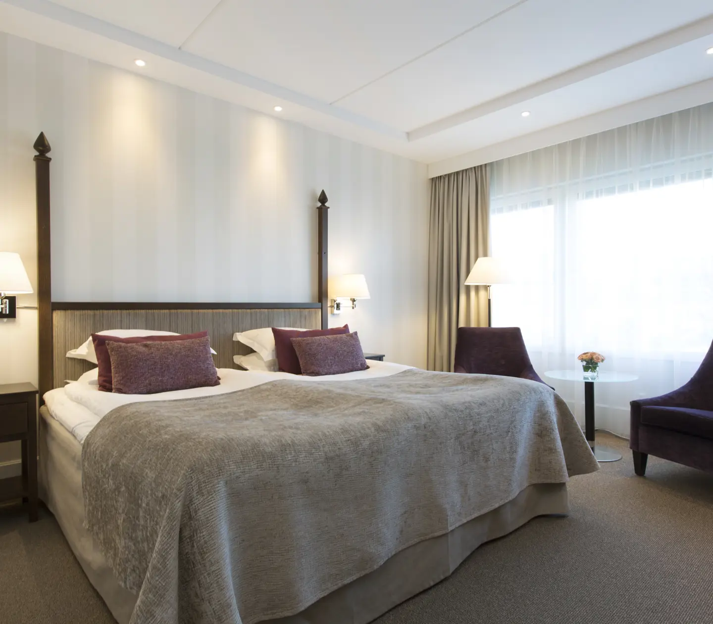 Ljust hotellrum med säng, fåtöljer och fönster