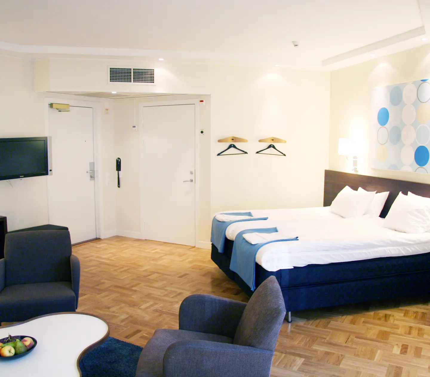 Ljust hotellrum med säng, fåtöljer och tv