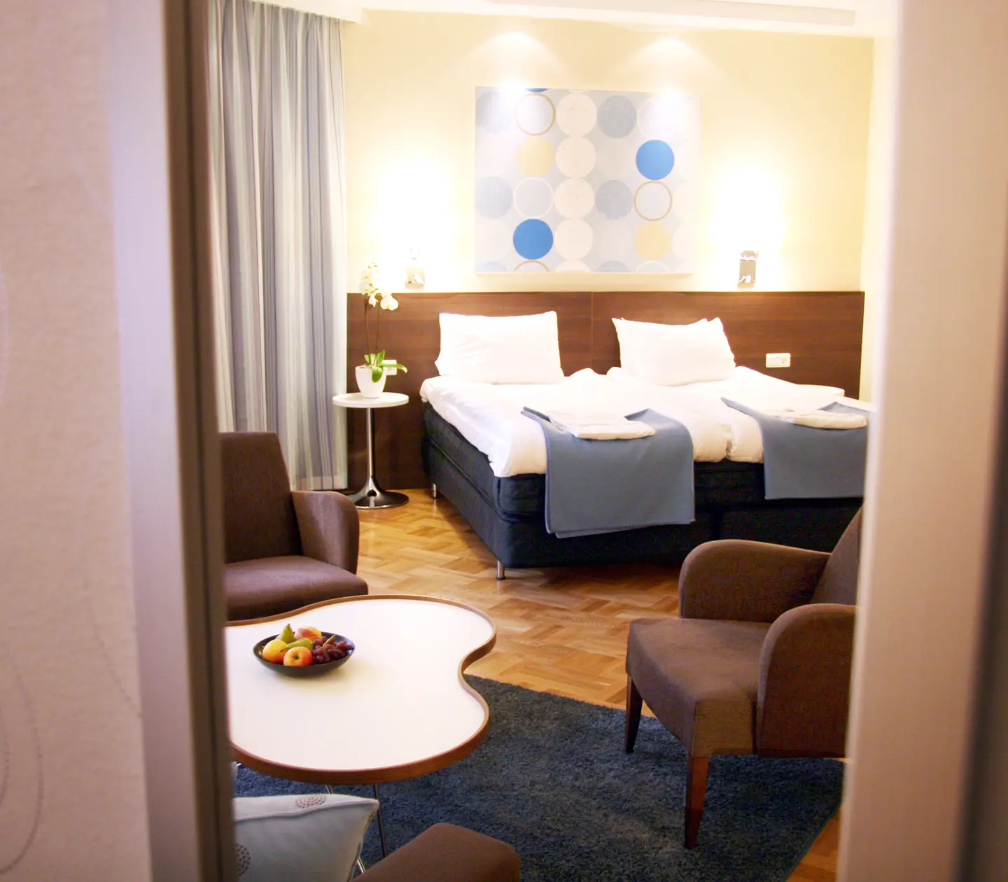 Ljust hotellrum med säng, fåtöljer och tavla