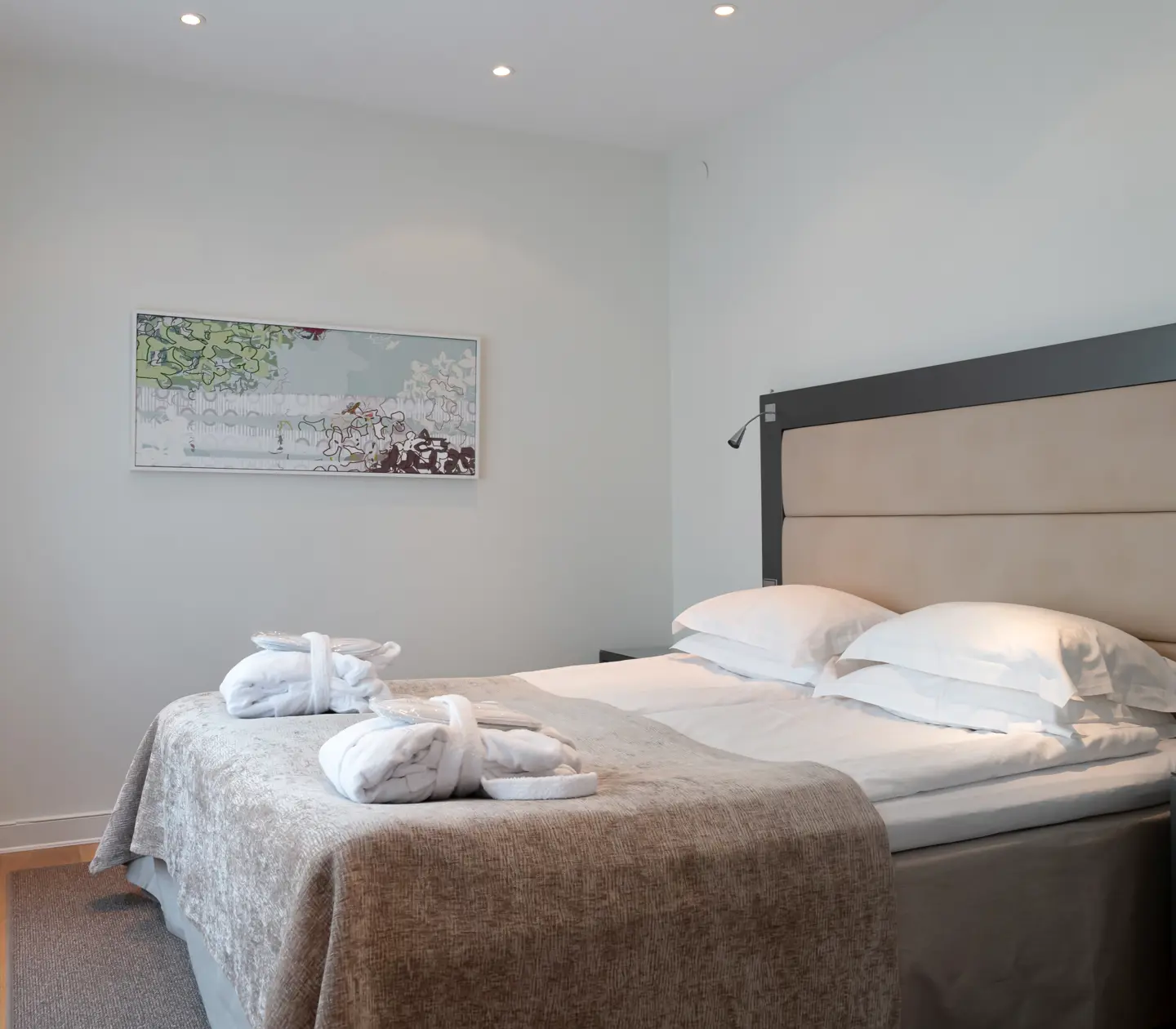 Ljus hotellsvit med säng, sänggavel och morgonrockar