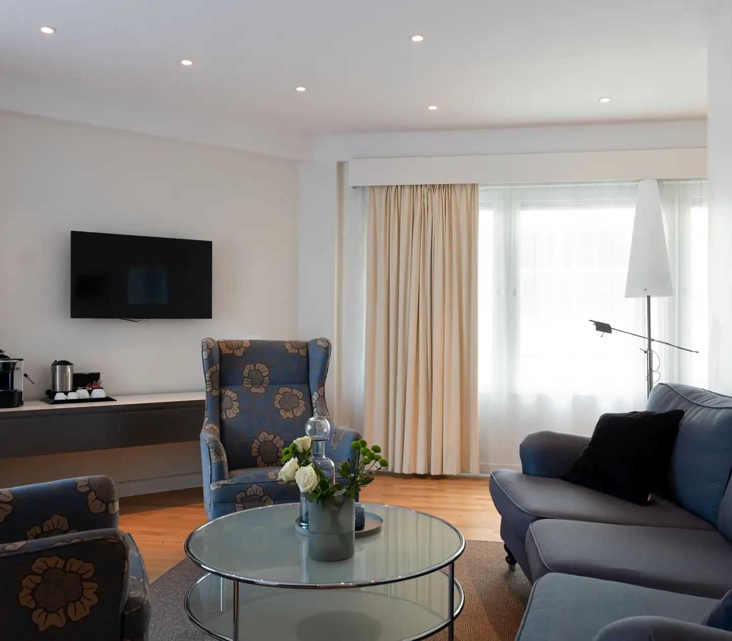Ljus hotellsvit med soffgrupp, tv och fönster