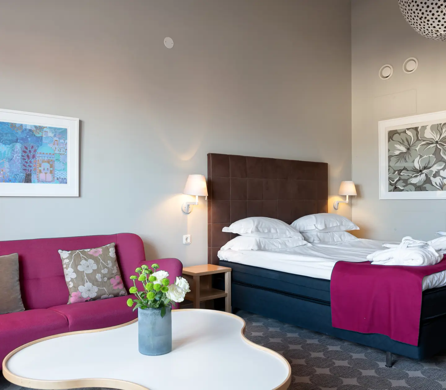 Ljus hotellsvit med soffa, säng och mörk sänggavel