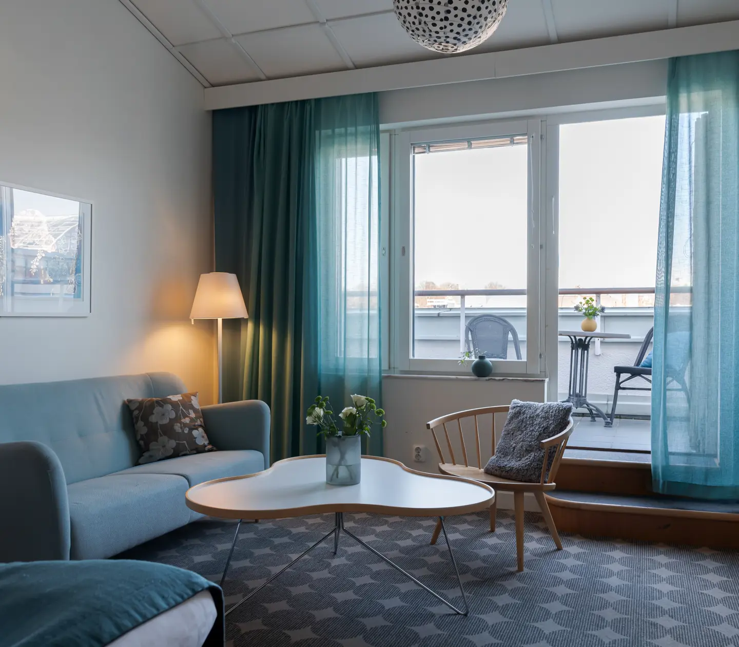 Ljus hotellsvit med soffa, balkong och blå gardiner
