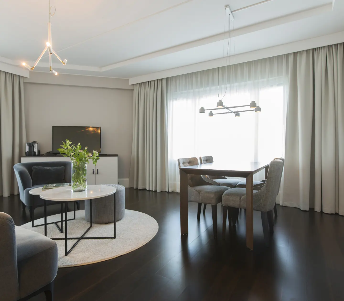 Ljus hotellsvit med soffgrupp, matgrupp och fönster