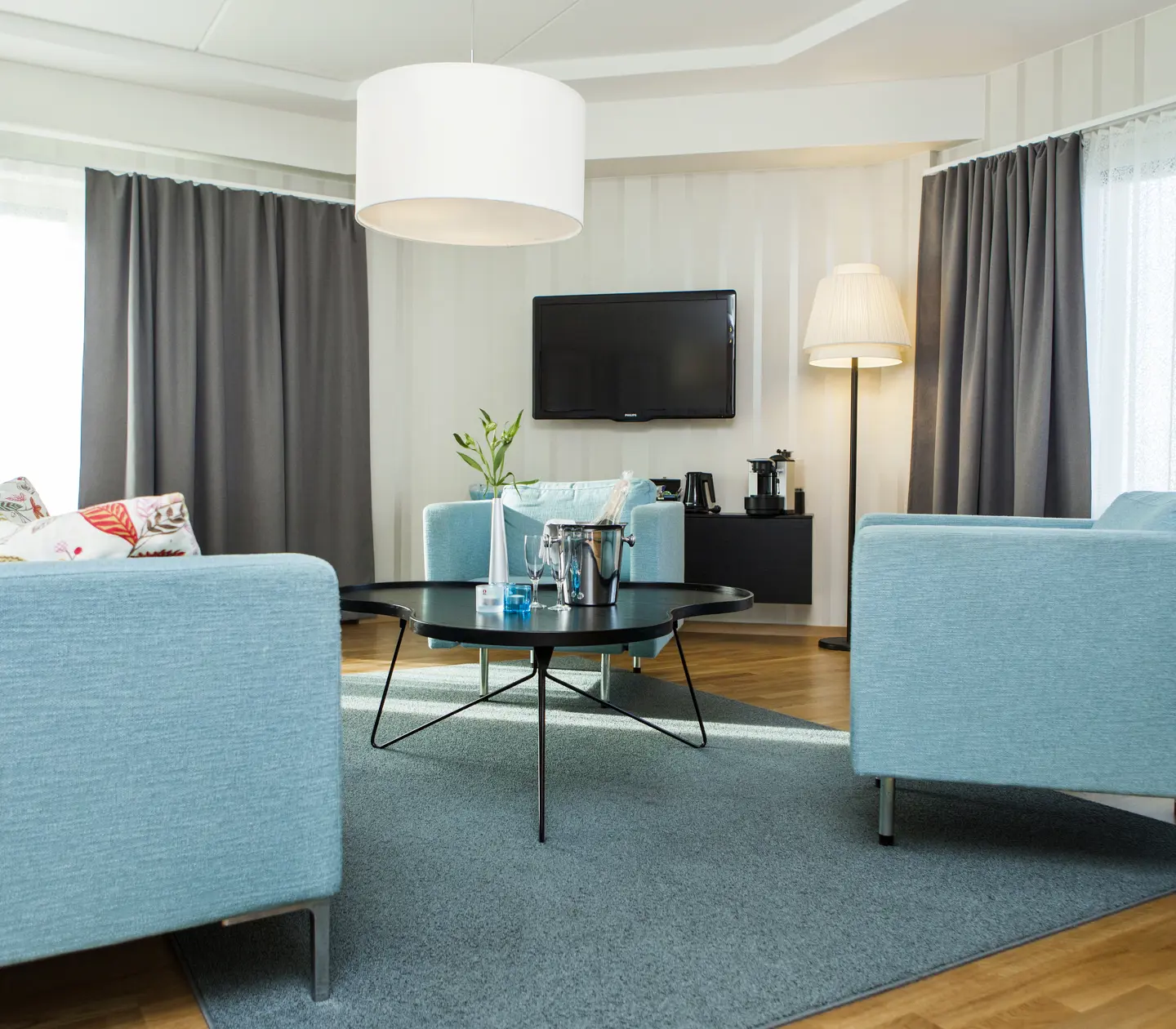 Ljus hotellsvit med blå soffgrupp, fönster och tv