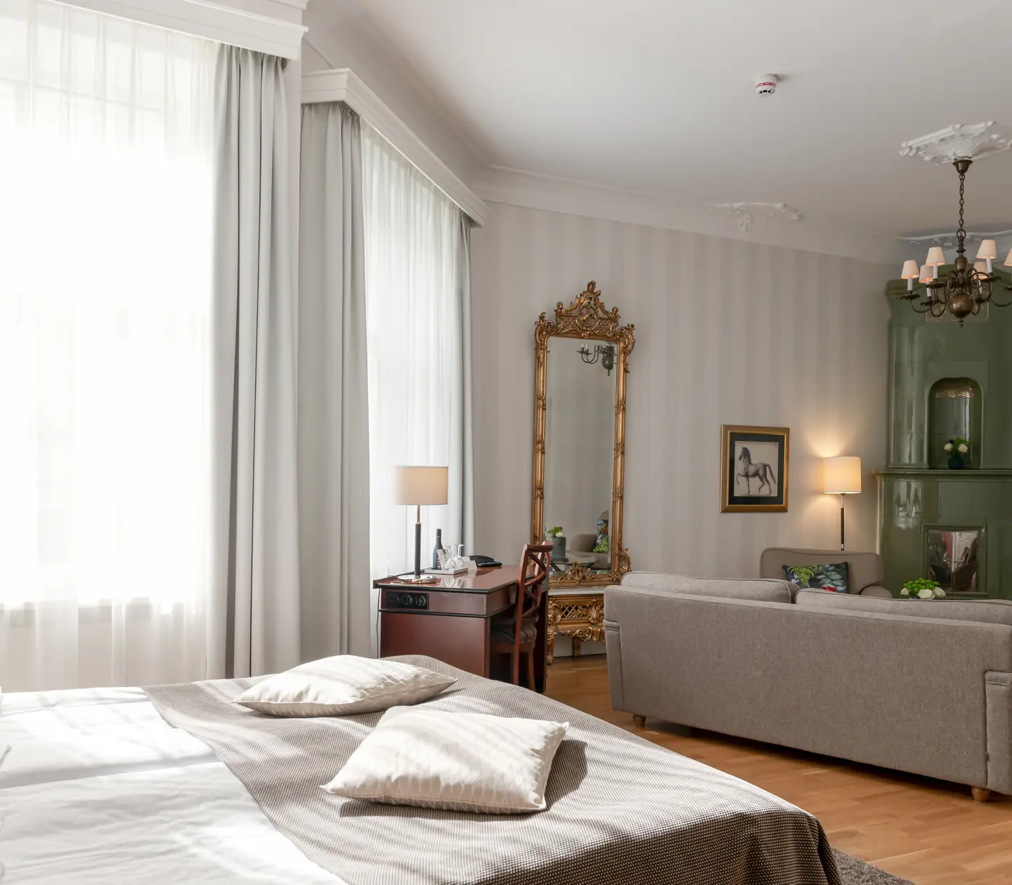 Ljust hotellrum med grön kakelugn, säng och stora fönster