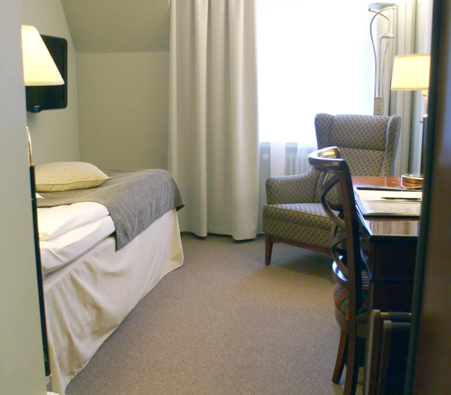 Hotellrum med enkelsäng, fåtölj och skrivbord