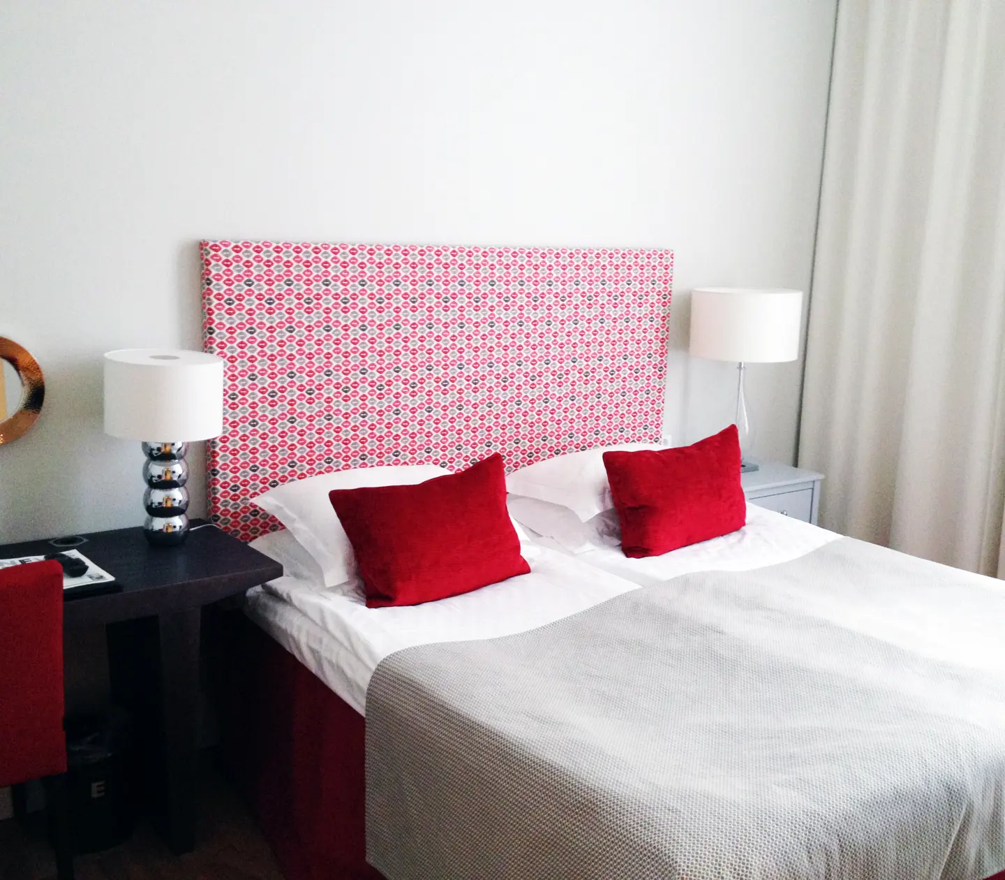 Hotellrum med dubbelsäng, röd sänggavel och skrivbord