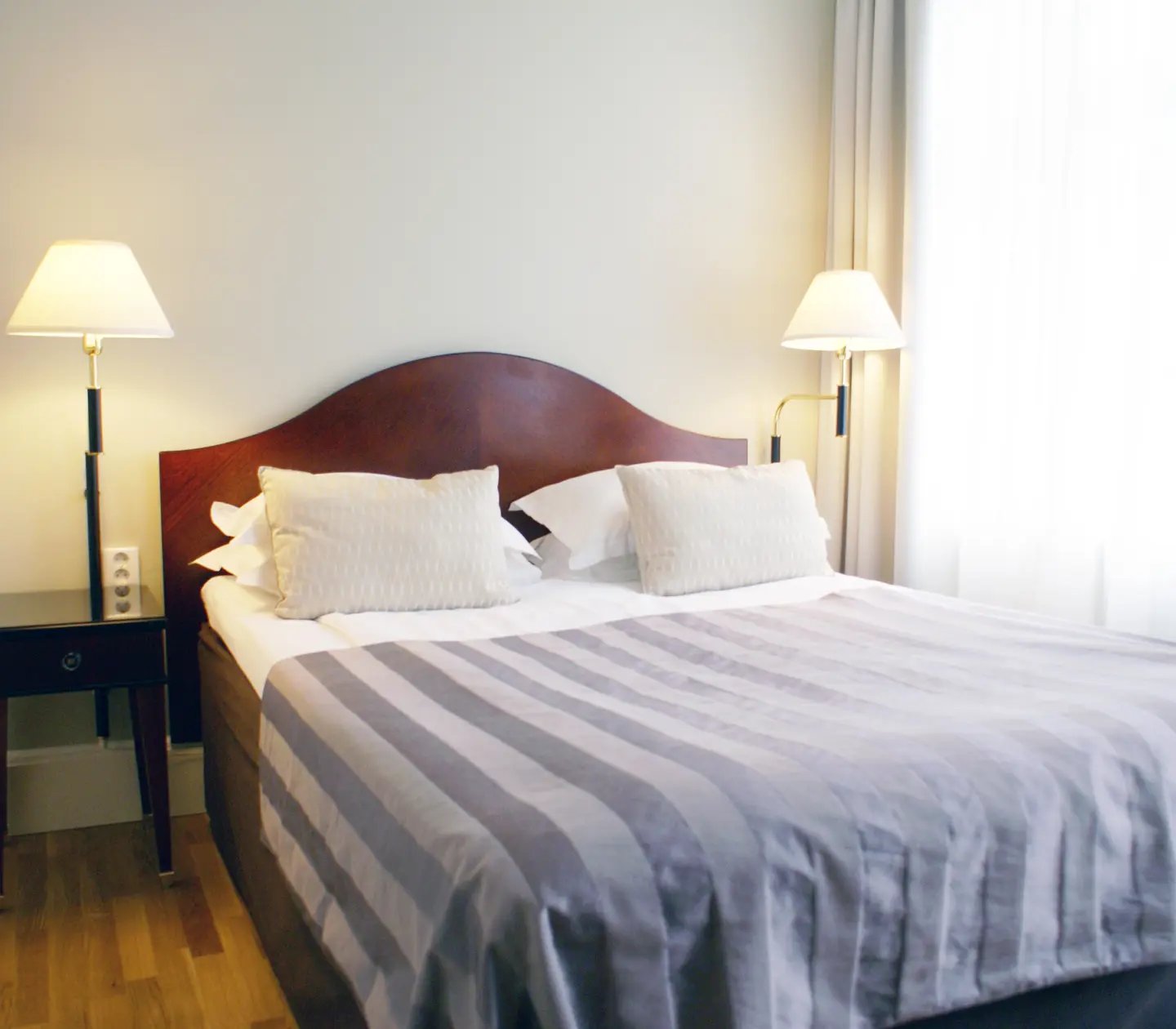 Hotellrum med dubbelsäng, sänglampor och gardiner