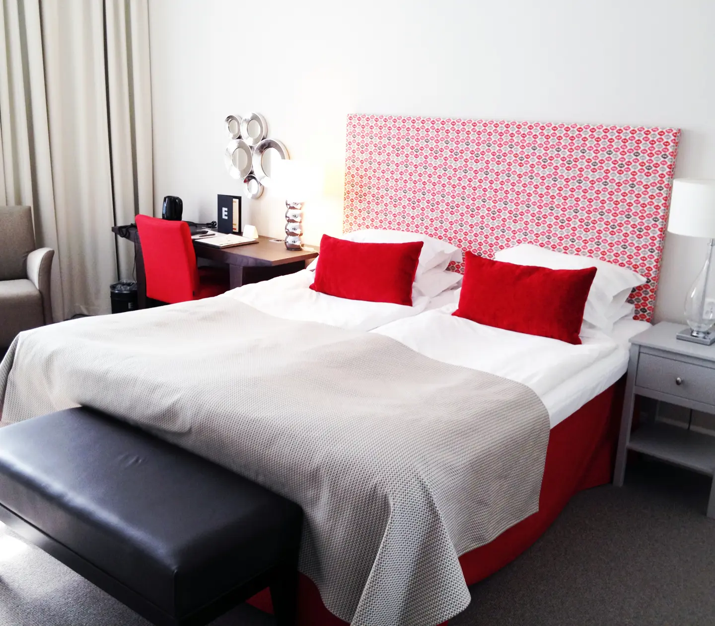 Hotellrum med dubbelsäng, röd sänggavel och skrivbord