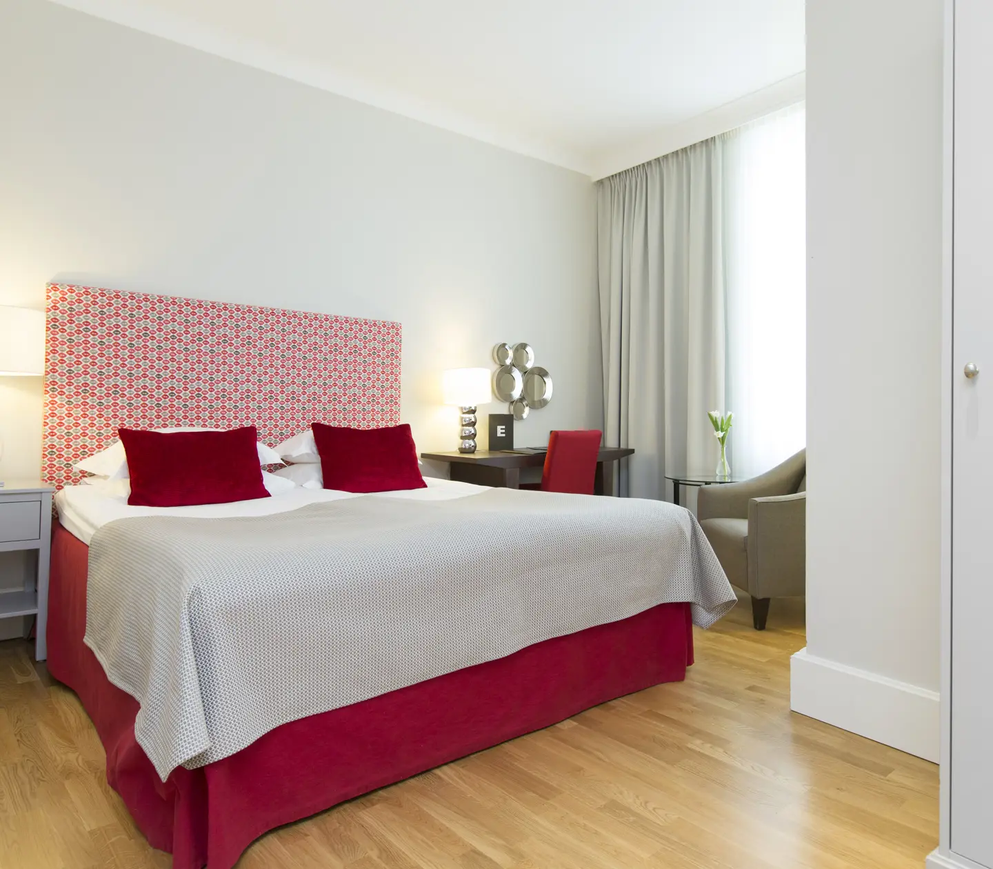 Hotellrum med dubbelsäng, röd sänggavel och skrivbord