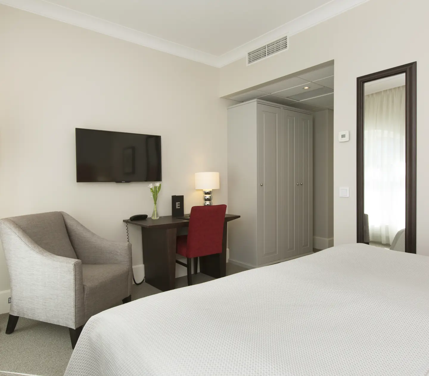 Ljust hotellrum med dubbelsäng, skrivbord och fåtölj