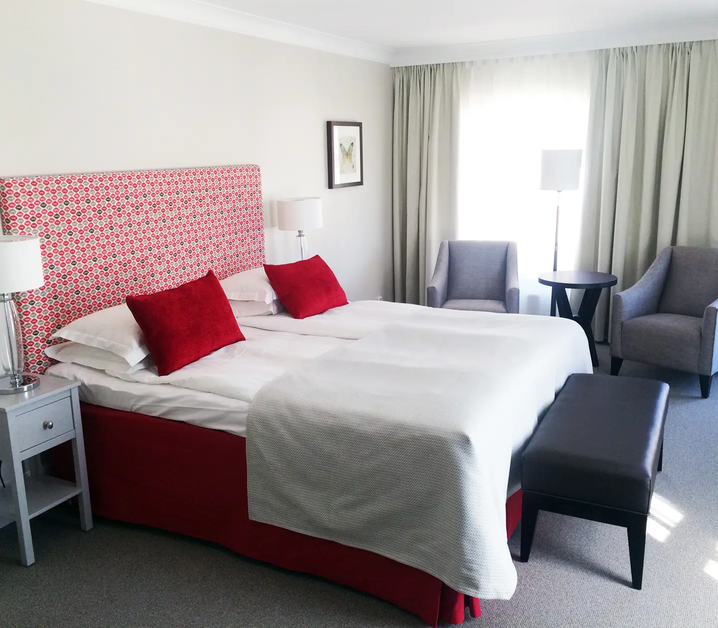 Hotel room with double bed, red headboard and armchairs
