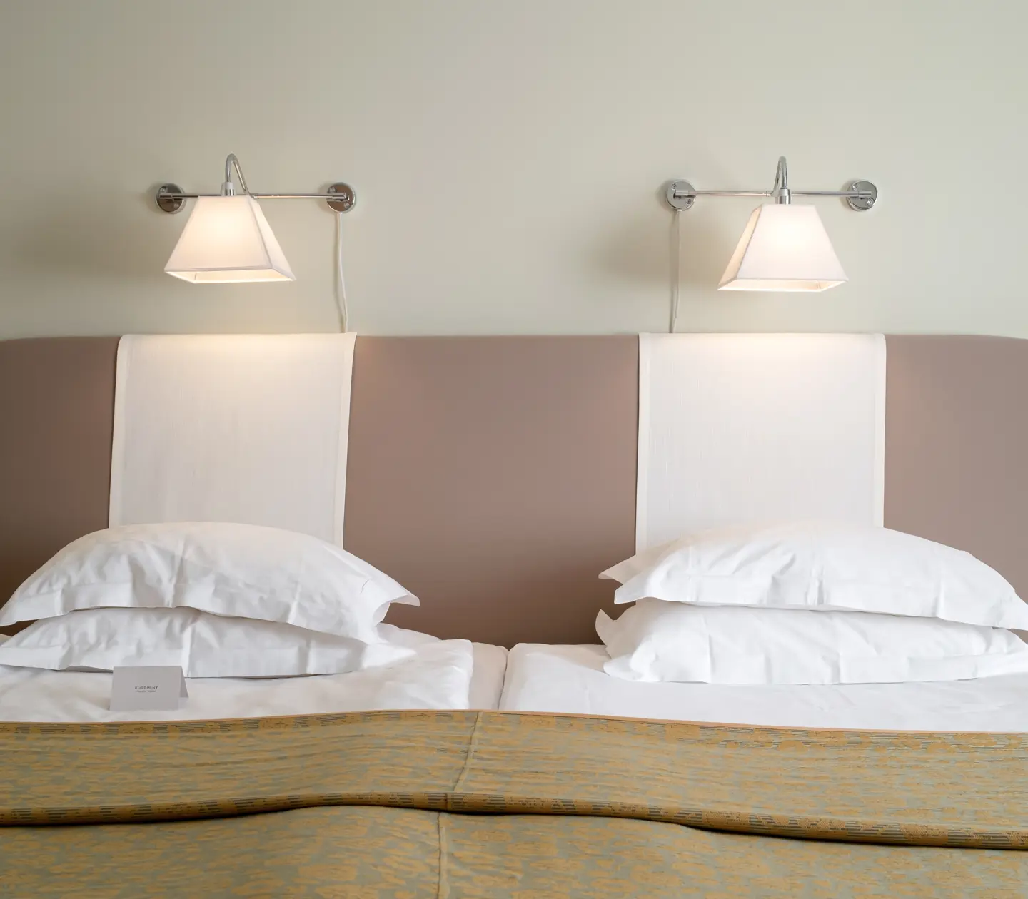 Hotellrum med säng, sänglamor och vita kuddar