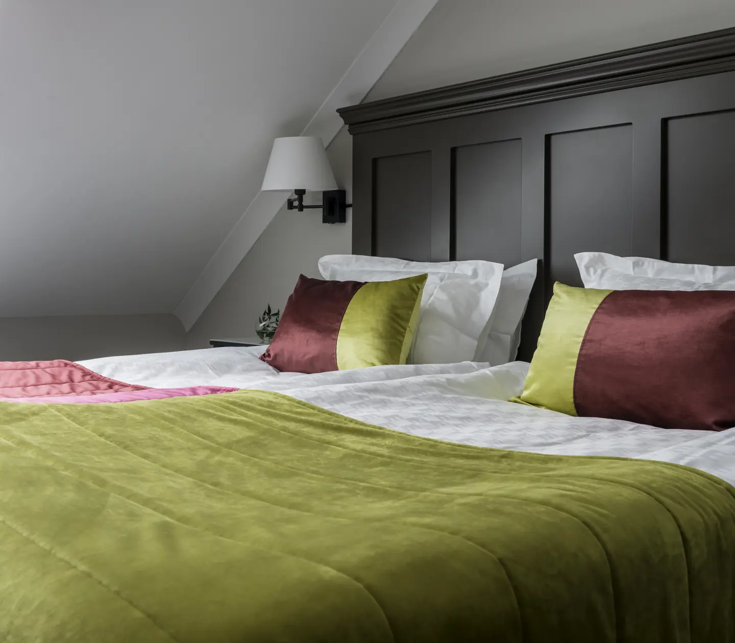 Hotellrum med säng, stor sänggavel i trä och snedtak