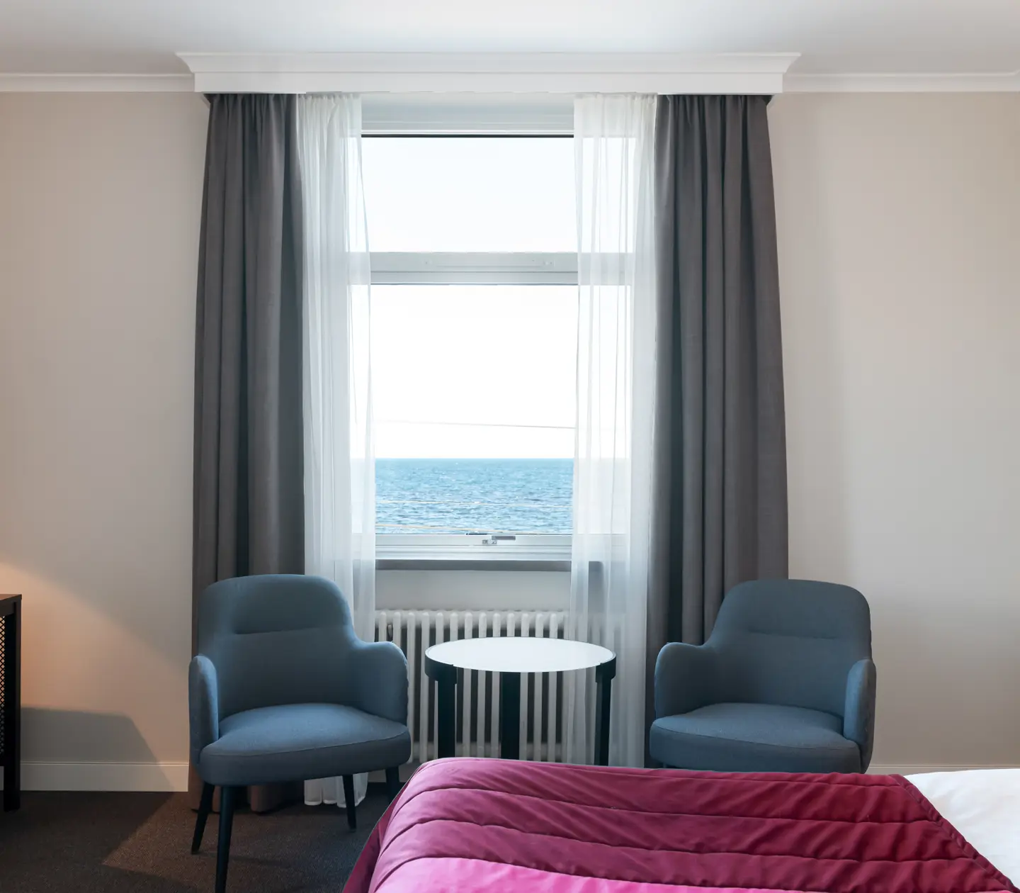 Hotellrum med säng, fåtöljer och havsutsikt