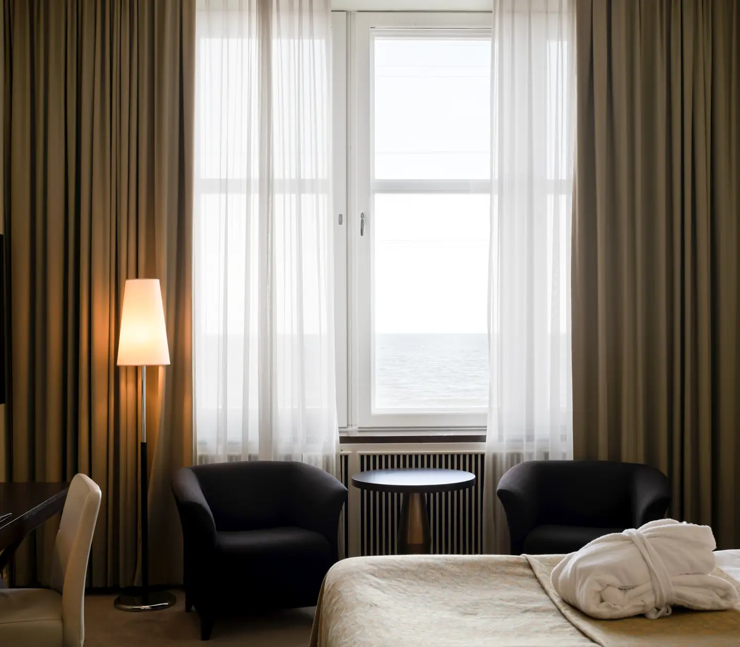 Hotellrum med säng, fåtöljer och havsutsikt