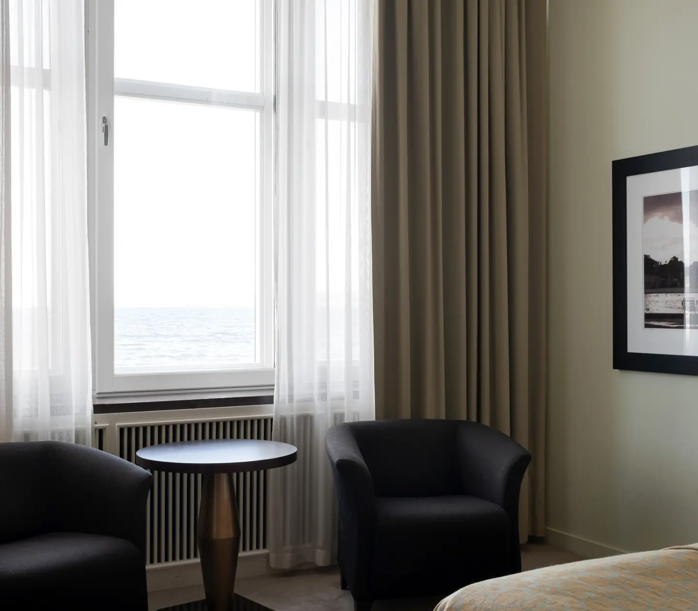 Hotellrum med fåtöljer, tavla och havsutsikt