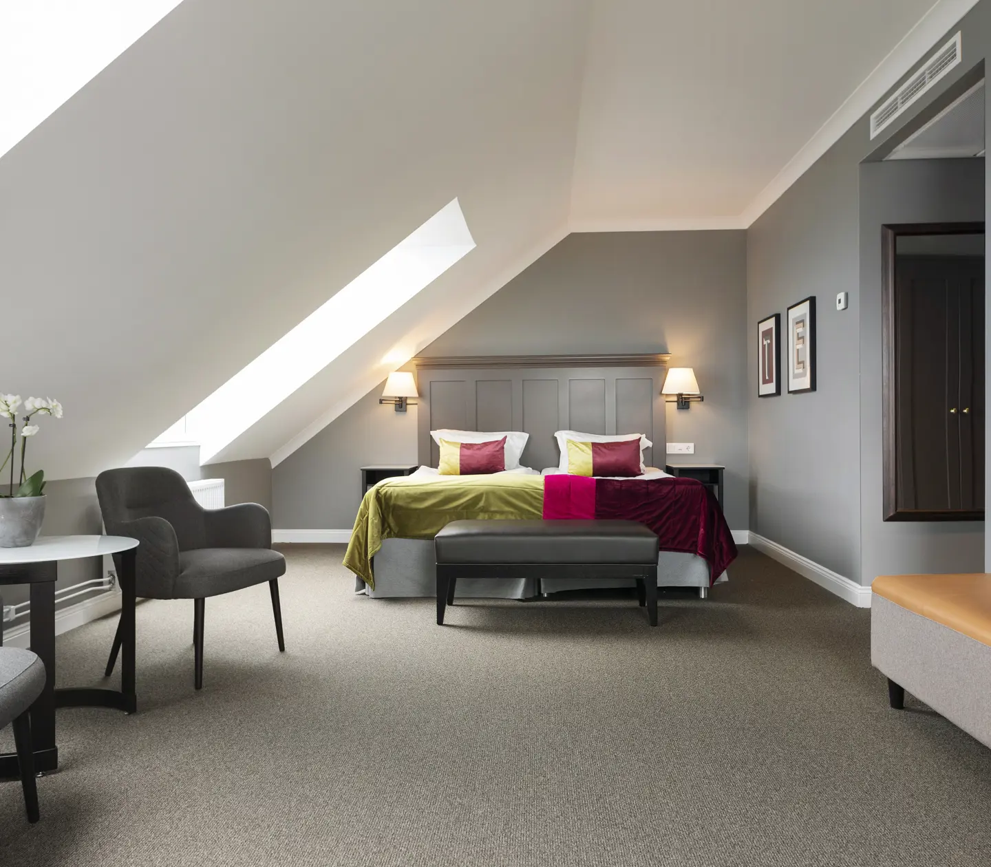 Hotellrum med säng, fåtöljer och snedtak