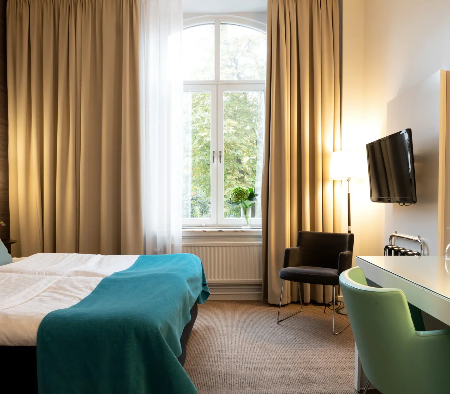 Hotellrum med dubbelsäng, skrivbord och stort fönster