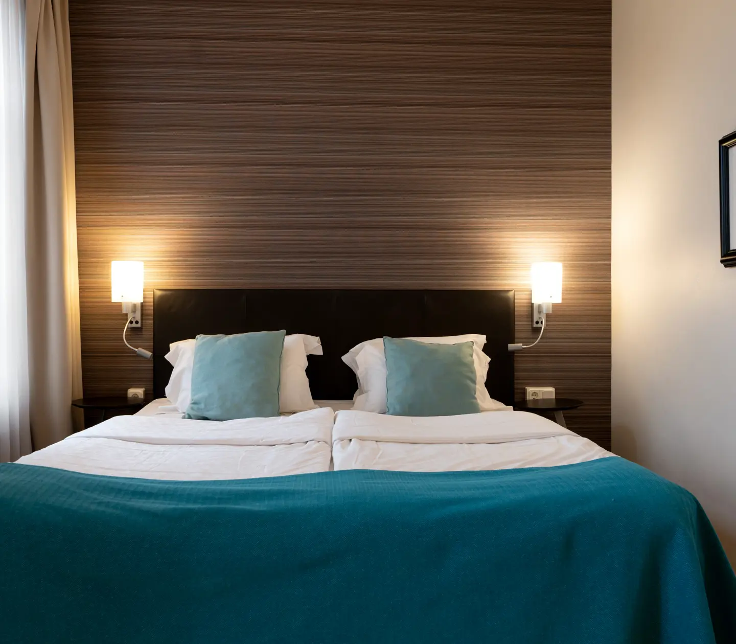 Hotellrum med dubbelsäng, sänglampor och fönster