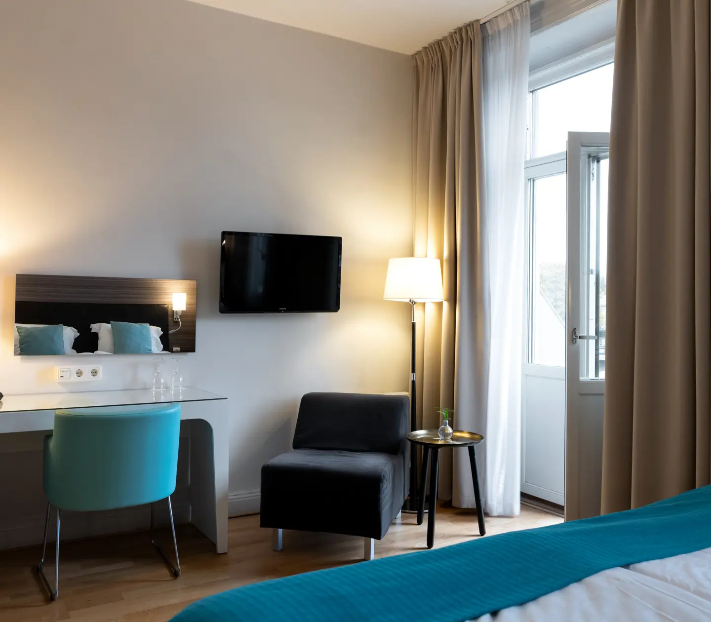 Hotellrum med dubbelsäng, skrivbord och balkongdörr