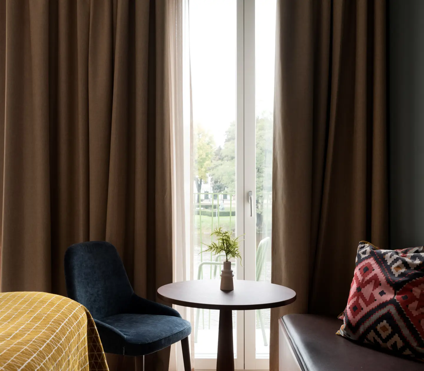 Ombonat hotellrum med varma textiler och stora fönster mot balkong