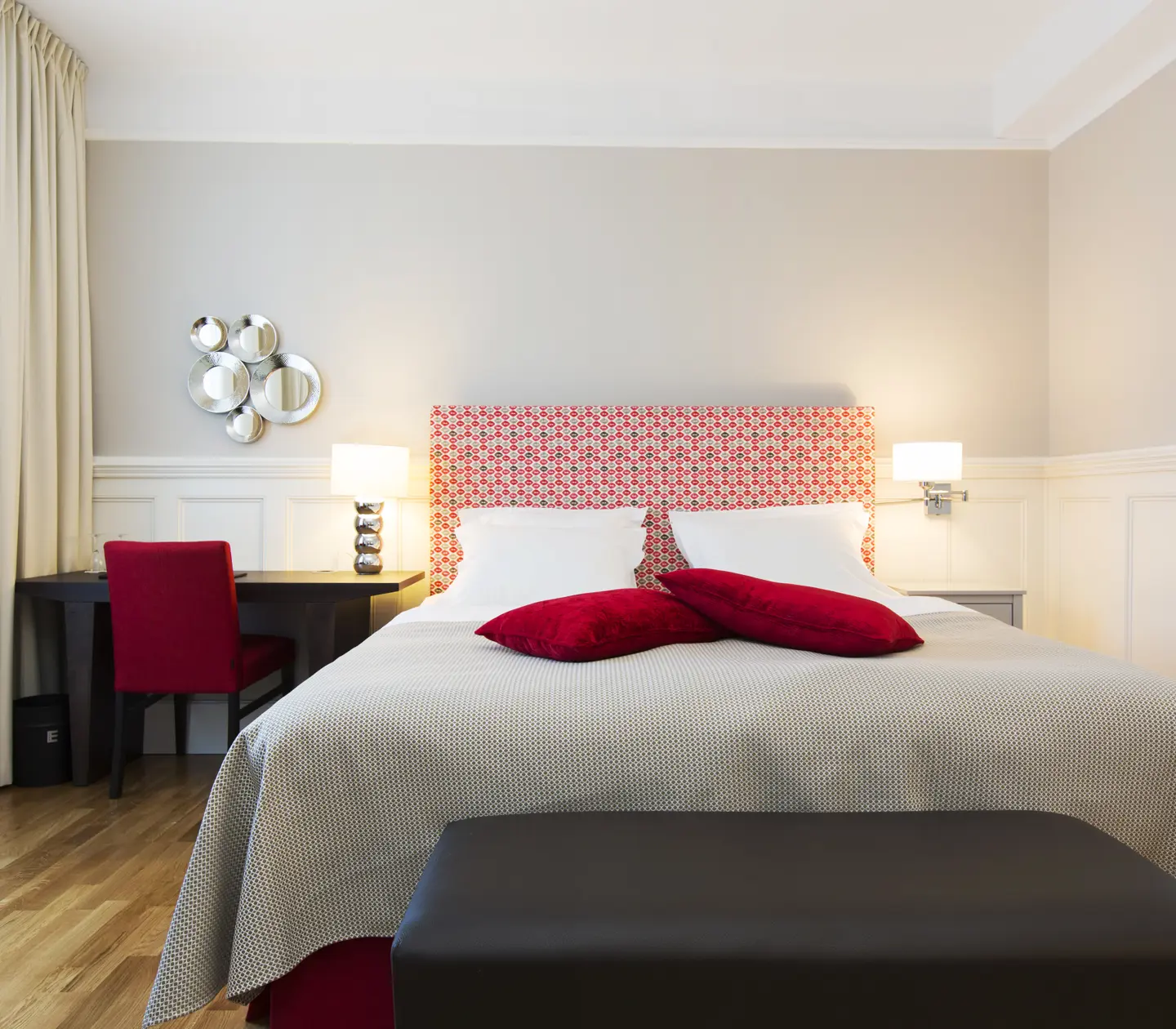 Ljust hotellrum med säng, röd sänggavel och skrivbord