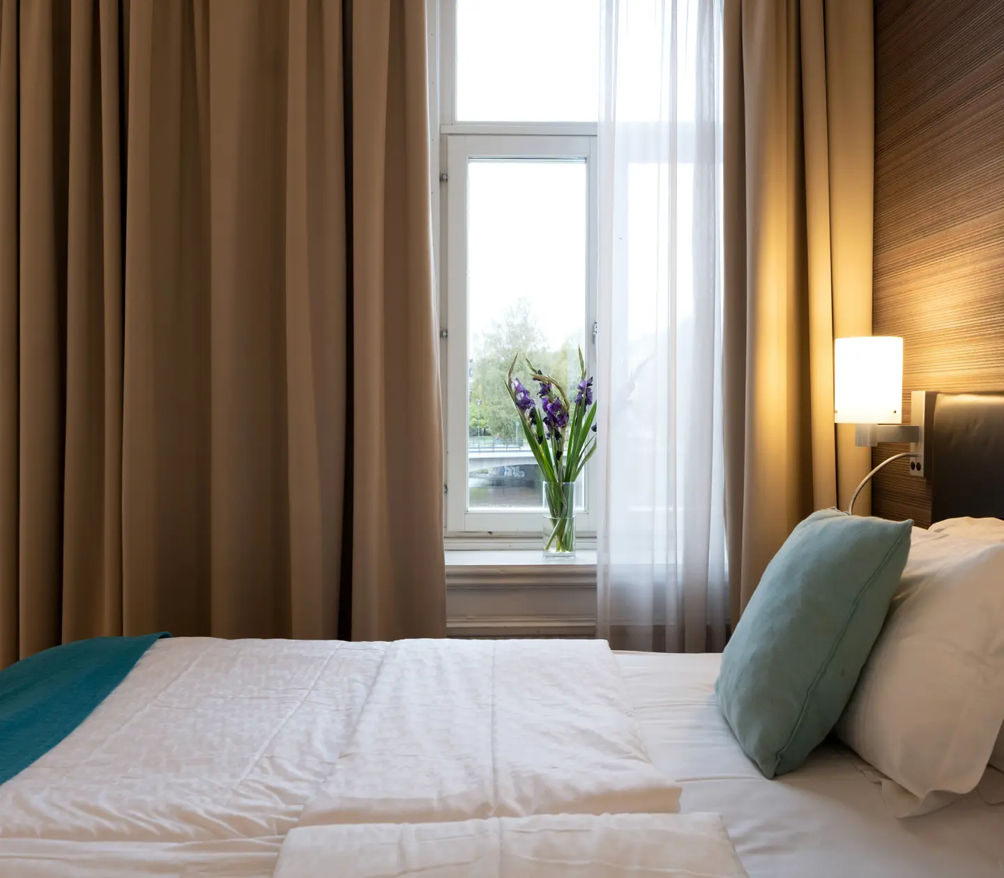 Ombonat hotellrum med dubbelsäng, varma textiler och stora fönster