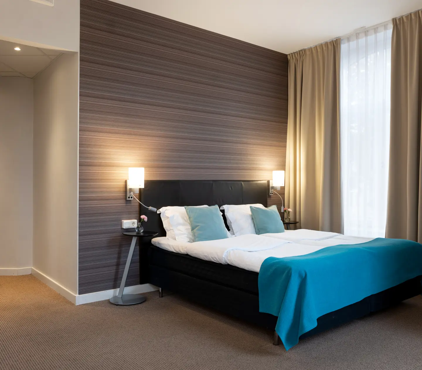 Ombonat hotellrum med dubbelsäng, varma textiler och stora fönster