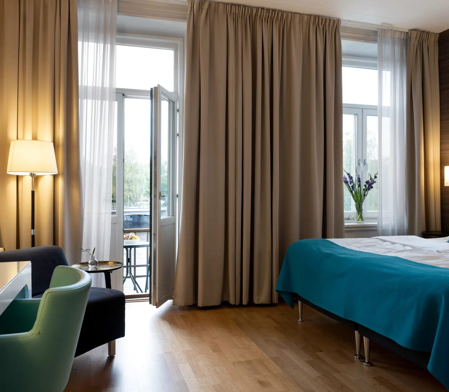 Ombonat hotellrum med dubbelsäng, skrivbord och balkongdörr