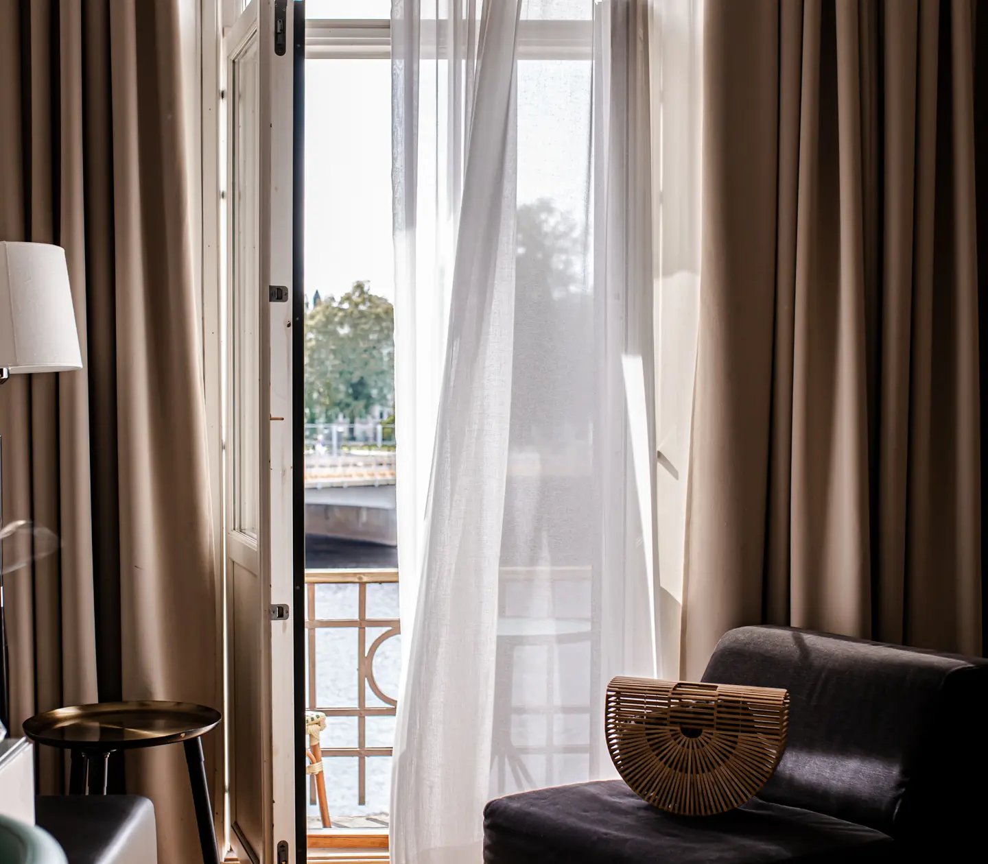 Ombonat hotellrum med öppen balkongdörr, varma textiler och väska
