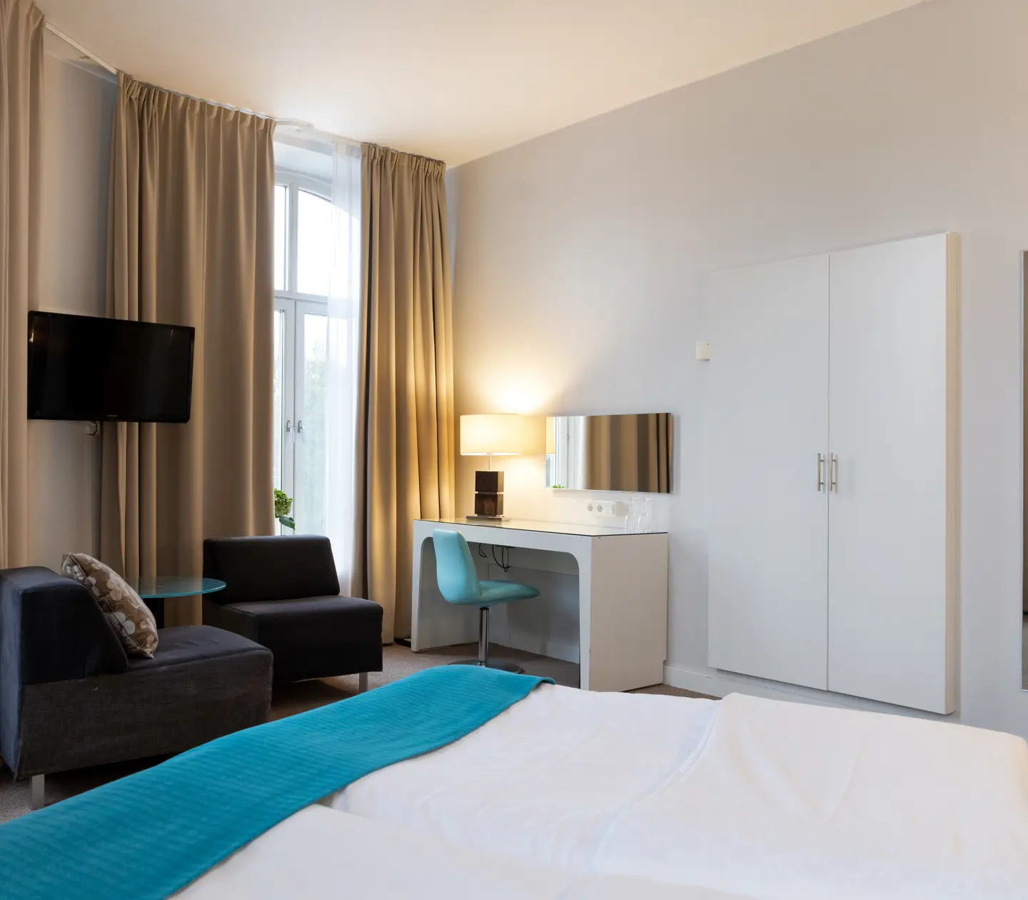 Ljust hotellrum med säng, skrivbord och fåtöljer