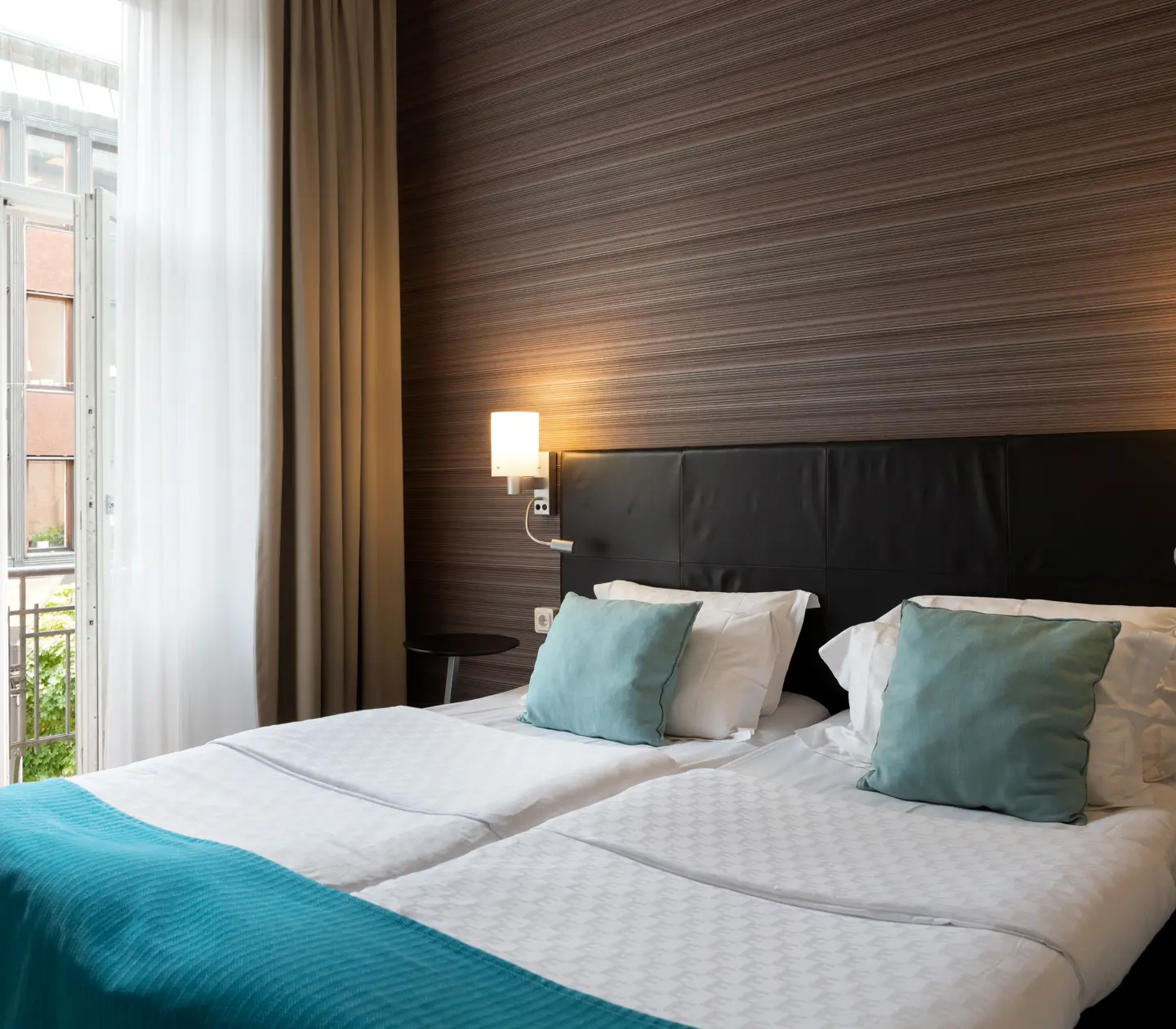 Hotellrum med dubbelsäng, sänglampor och öppen balkongdörr