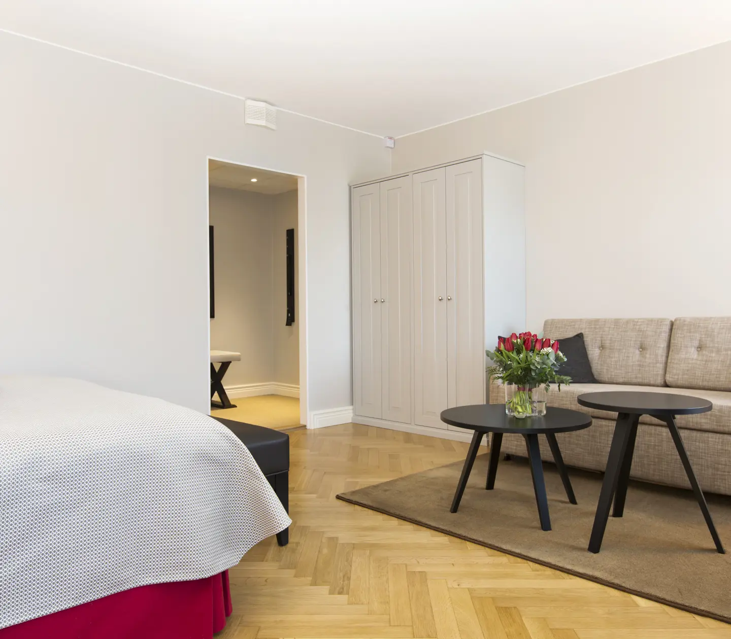 Ljust hotellrum med soffa, garderob och rosbukett