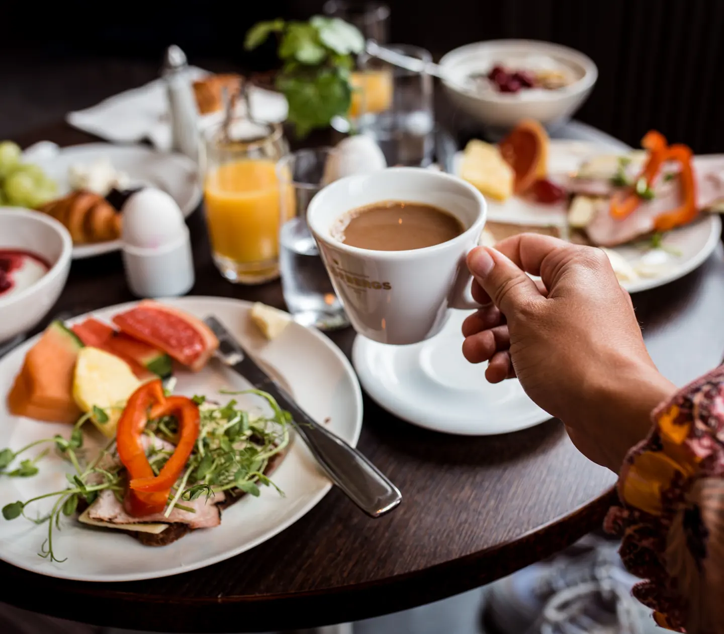 Frukostbuffé serverad på runt bord och hand som lyfter upp kaffekopp