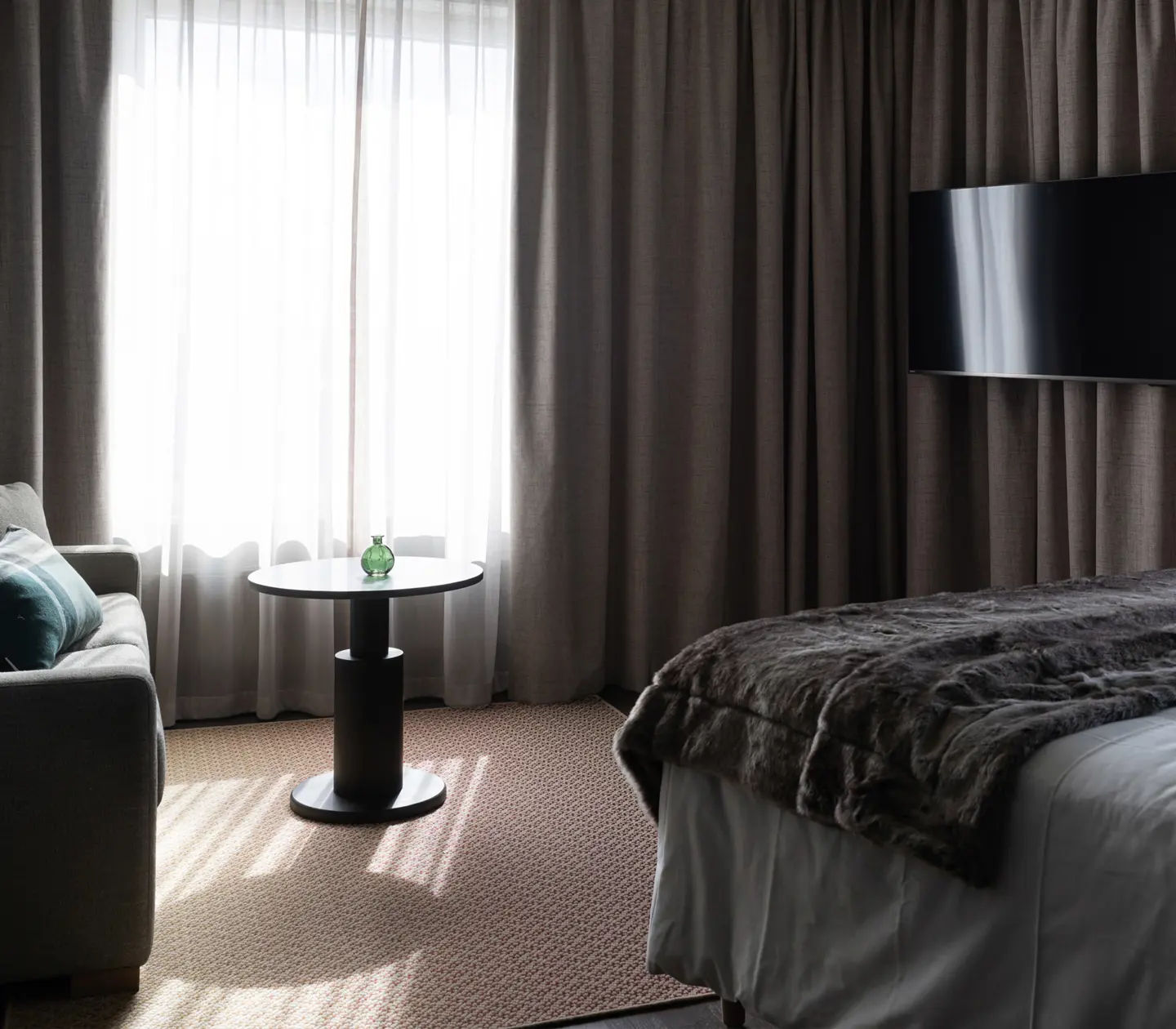 Modernt hotellrum med soffa, säng och TV, gardiner i bakgrunden