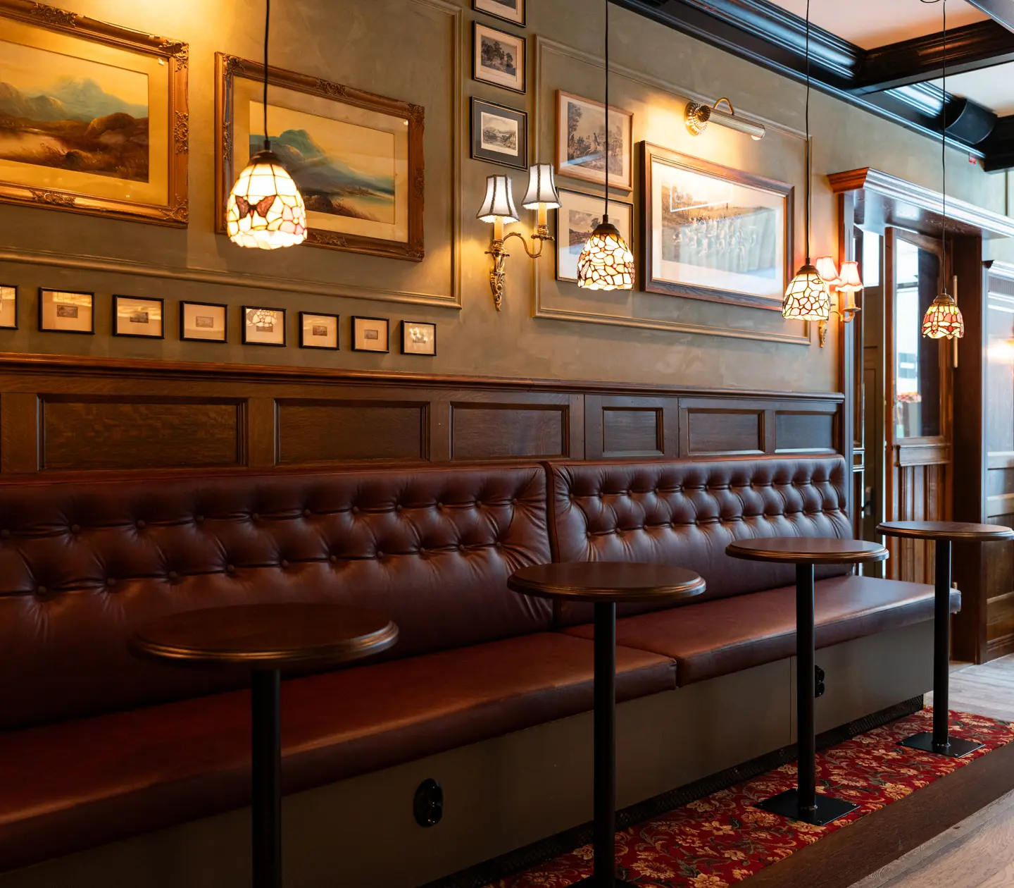 Sittplatser längst väggen på Bishop Arms i mörkt läder och nätta barbord