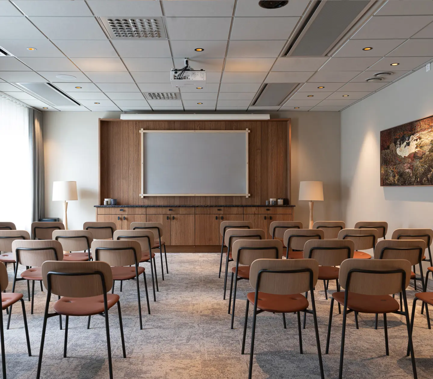 Konferenssal med stolar i biosittning och en skärm med träram