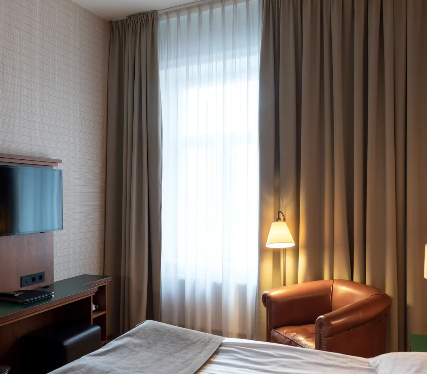 Hotellrum med säng, läderfåtölj och fönster