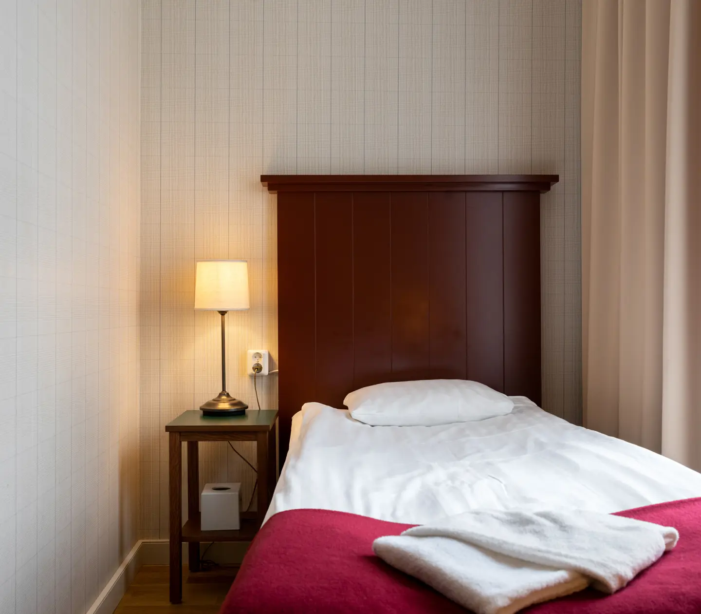 Mysigt hotellrum med säng, sänggavel i trä och sänglampa