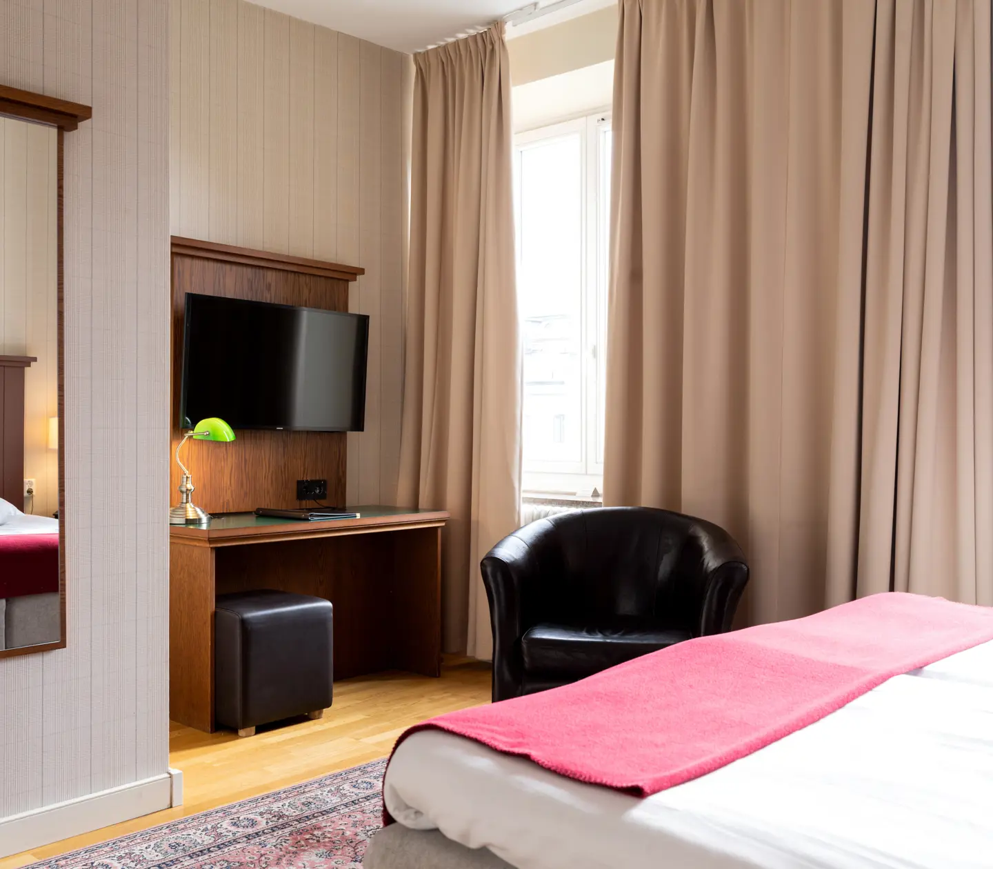Mysigt hotellrum med skrivbord, spegel och svart läderfåtölj