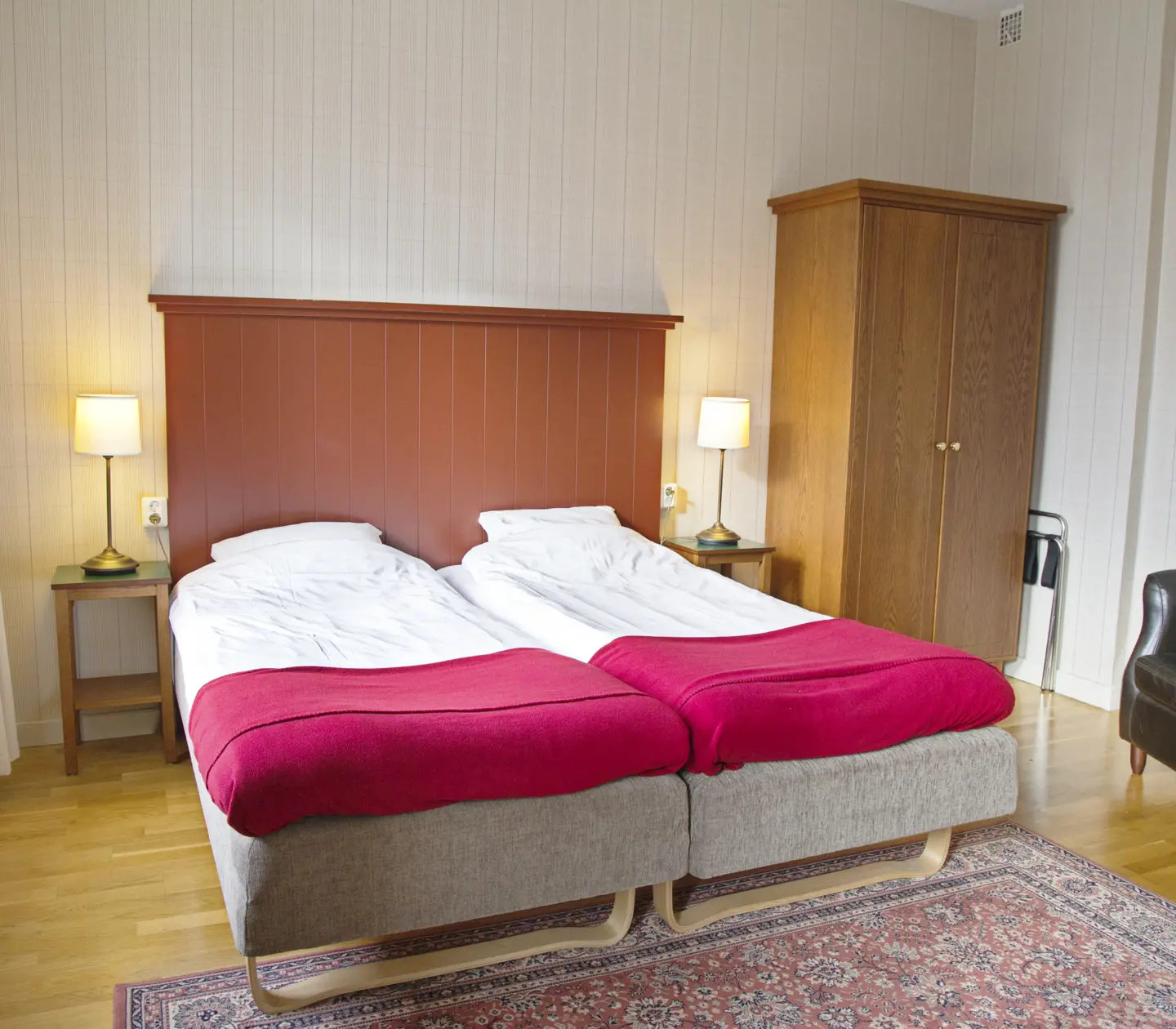 Mysigt hotellrum med säng, svart läderfåtölj och garderob