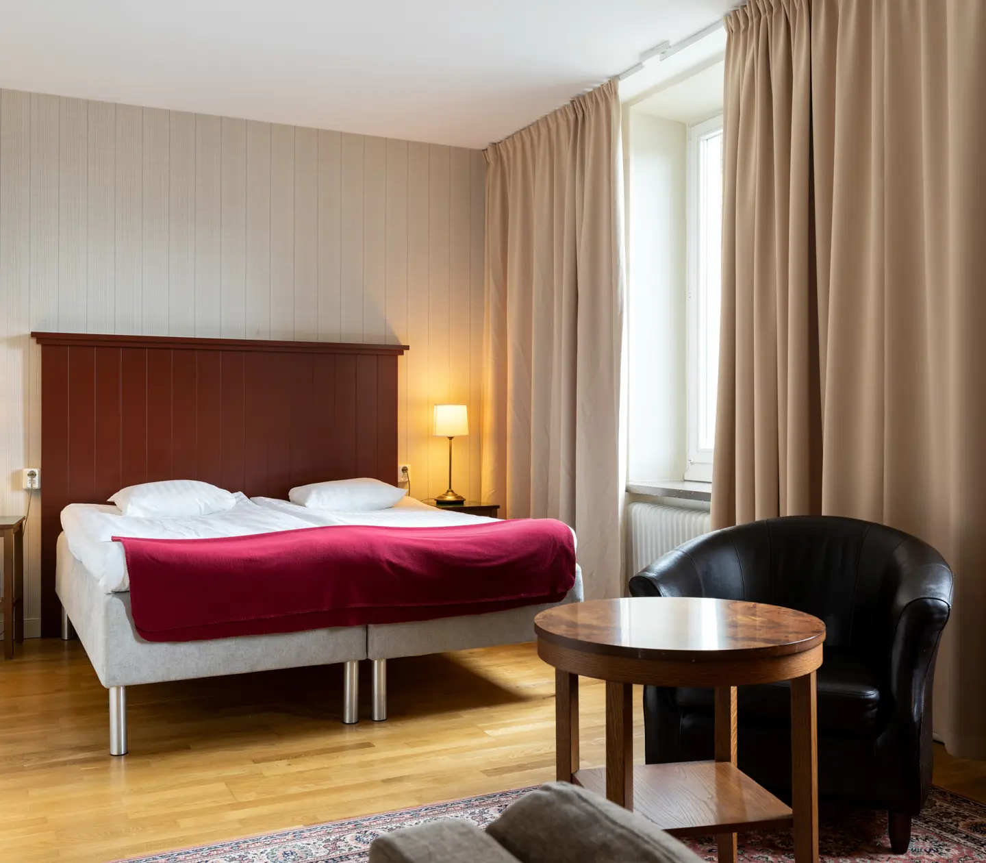 Mysigt hotellrum med säng, sänggavel i trä och svart läderfåtölj